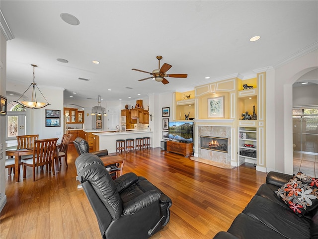 living room featuring crown molding, ceiling fan, a fireplace, built in shelves, and light wood-type flooring