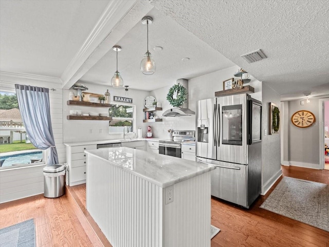 kitchen featuring light wood-type flooring, white cabinets, pendant lighting, stainless steel appliances, and wall chimney range hood