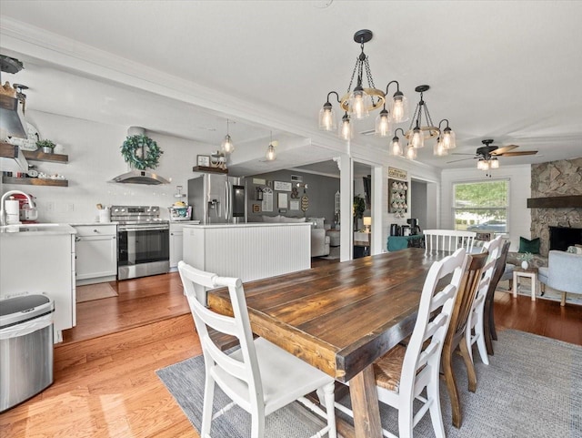 dining space with ceiling fan with notable chandelier, sink, a fireplace, and light hardwood / wood-style floors