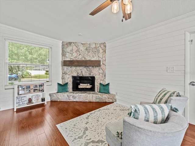 living room with hardwood / wood-style flooring, ornamental molding, and a stone fireplace