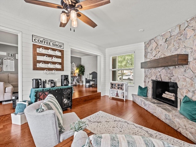 living room featuring wood-type flooring, ornamental molding, ceiling fan, and a fireplace