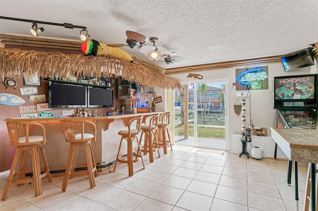 kitchen featuring light tile patterned floors, rail lighting, a textured ceiling, a kitchen bar, and kitchen peninsula