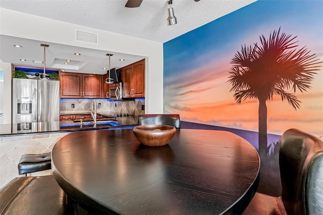 dining area featuring ceiling fan, a tray ceiling, sink, and a textured ceiling