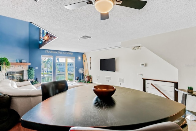 dining space with ceiling fan, a fireplace, and a textured ceiling