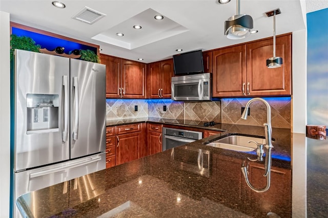 kitchen featuring sink, stainless steel appliances, tasteful backsplash, decorative light fixtures, and dark stone counters