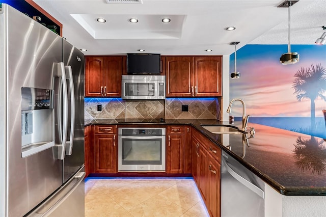 kitchen featuring decorative light fixtures, sink, dark stone counters, a tray ceiling, and stainless steel appliances