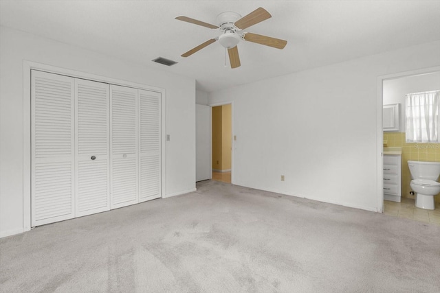 unfurnished bedroom with connected bathroom, tile walls, ceiling fan, light carpet, and a closet