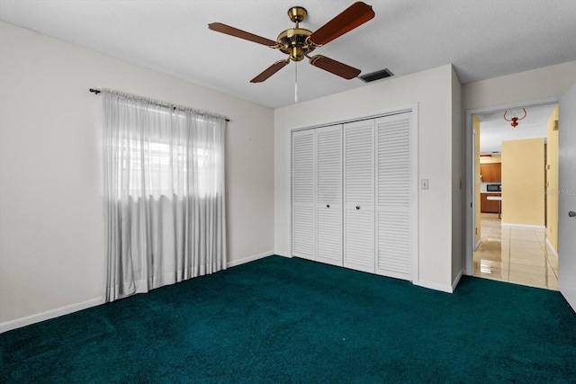 unfurnished bedroom with dark colored carpet, a textured ceiling, ceiling fan, and a closet