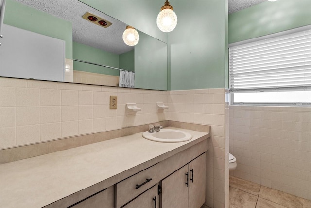 bathroom with tile walls, vanity, toilet, tile patterned floors, and a textured ceiling