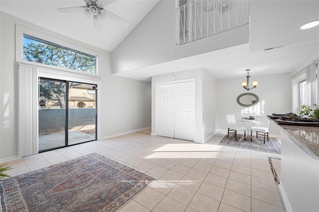 interior space featuring high vaulted ceiling, ceiling fan with notable chandelier, baseboards, and light tile patterned floors