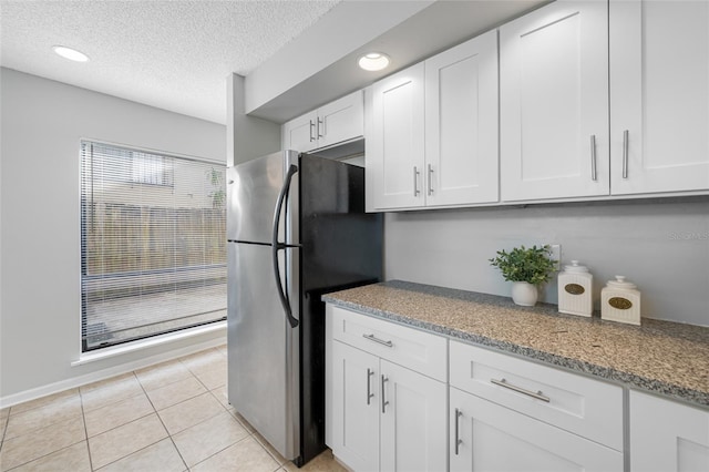 kitchen with freestanding refrigerator, white cabinets, a textured ceiling, and light tile patterned flooring