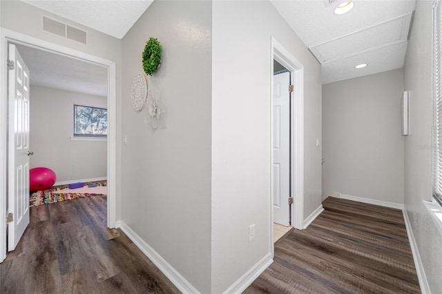 hallway featuring baseboards, visible vents, dark wood finished floors, and attic access