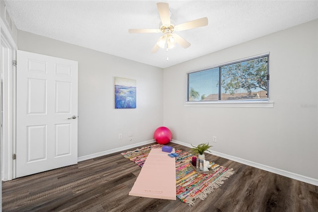 exercise room with a textured ceiling, ceiling fan, dark wood finished floors, and baseboards