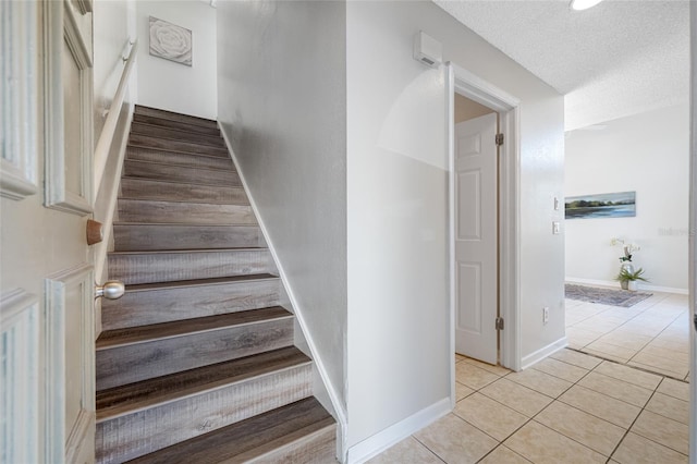 stairway with tile patterned flooring, baseboards, and a textured ceiling