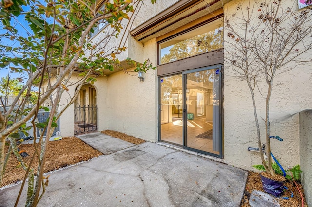 entrance to property with a patio area, a gate, and stucco siding