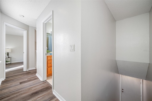 hallway with baseboards, a textured ceiling, and wood finished floors