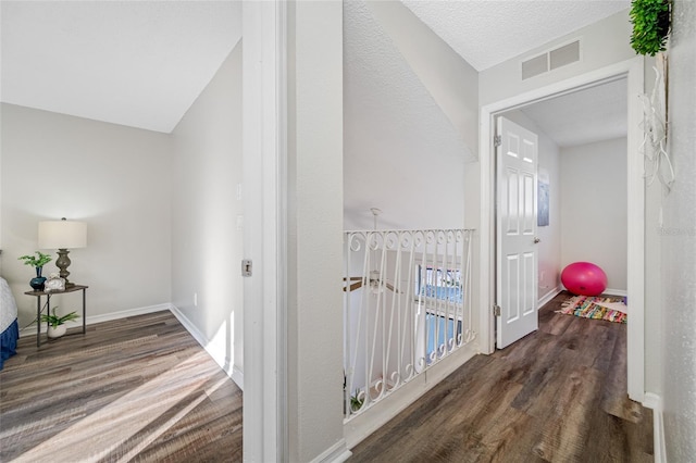 corridor featuring baseboards, a textured ceiling, visible vents, and dark wood-style flooring