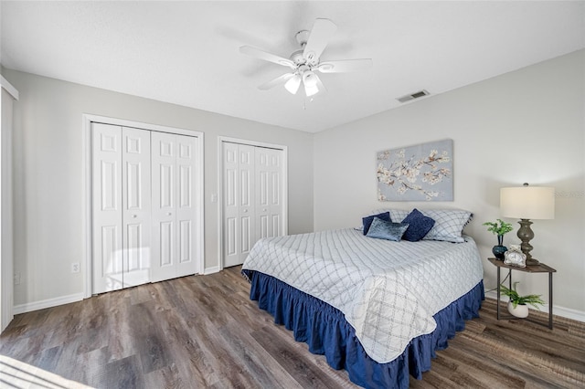 bedroom with dark wood-style flooring, multiple closets, visible vents, ceiling fan, and baseboards