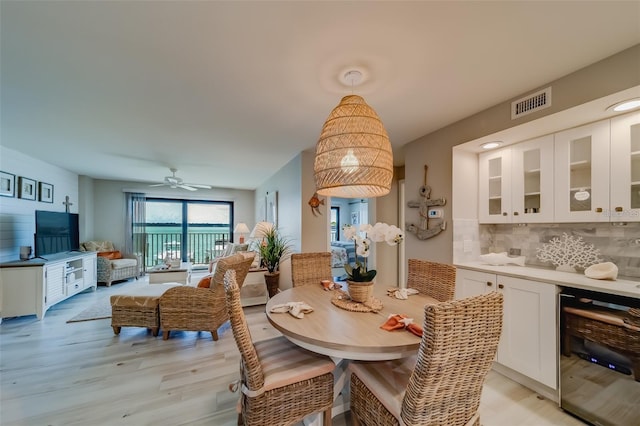 dining space featuring wine cooler, ceiling fan, and light wood-type flooring