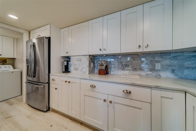 kitchen with stainless steel fridge, tasteful backsplash, light stone counters, white cabinets, and washer / clothes dryer