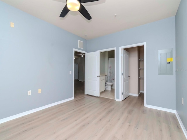 unfurnished bedroom with ensuite bathroom, a spacious closet, electric panel, a closet, and light hardwood / wood-style floors