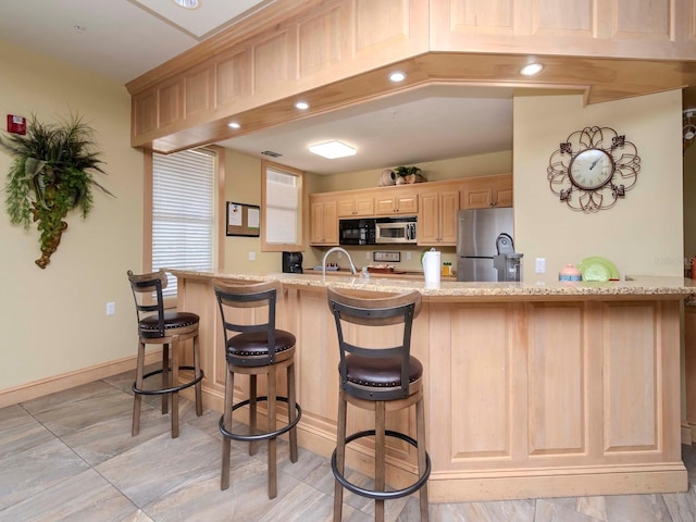 kitchen with light stone countertops, stainless steel appliances, kitchen peninsula, and light brown cabinets