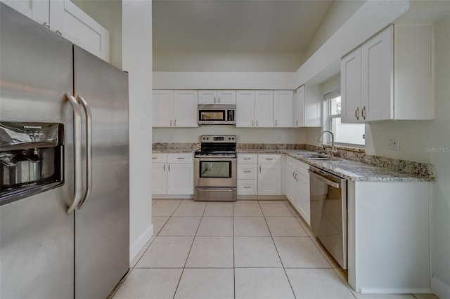 kitchen with appliances with stainless steel finishes, white cabinetry, sink, light tile patterned floors, and light stone countertops