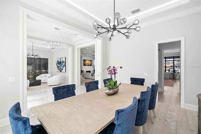 dining space featuring a raised ceiling, crown molding, light wood-type flooring, and a chandelier