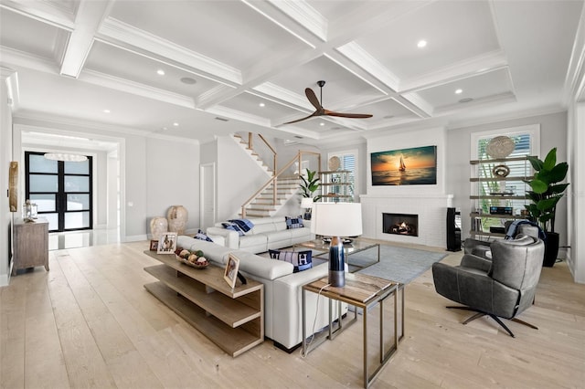 living room featuring beam ceiling, coffered ceiling, a fireplace, and light hardwood / wood-style flooring