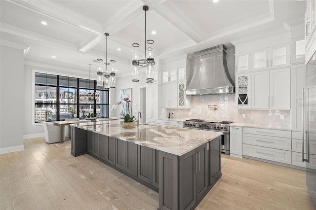 kitchen with a large island, white cabinets, wall chimney exhaust hood, and range with two ovens