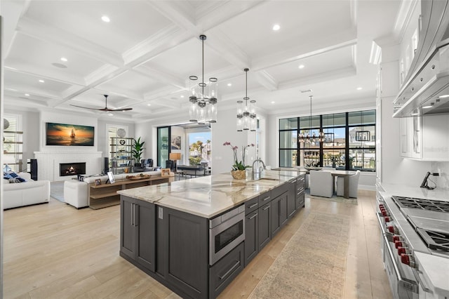 kitchen with a large island, appliances with stainless steel finishes, light stone counters, custom range hood, and decorative light fixtures