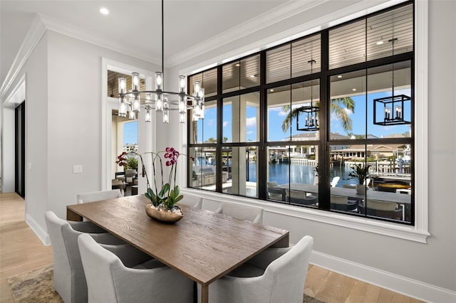 dining room featuring ornamental molding, a water view, an inviting chandelier, and light hardwood / wood-style floors