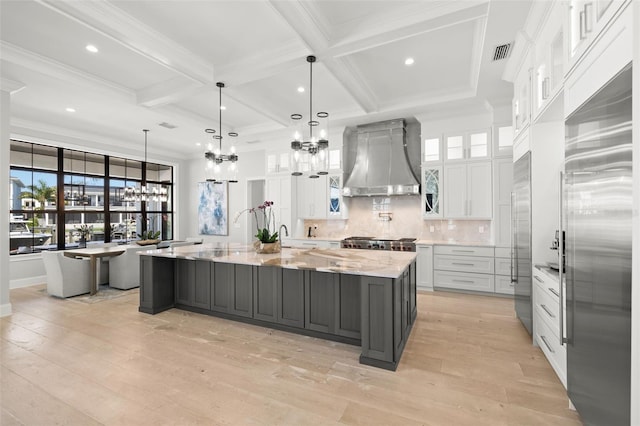 kitchen featuring pendant lighting, white cabinetry, a spacious island, light stone countertops, and wall chimney exhaust hood