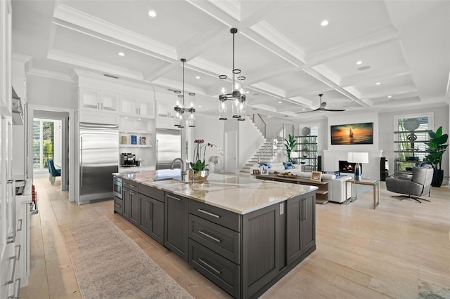 kitchen with sink, white cabinets, a large island with sink, stainless steel built in fridge, and light stone countertops