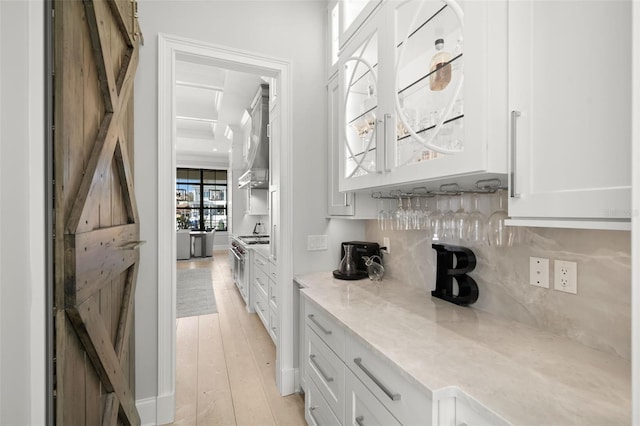 kitchen featuring high end stove, tasteful backsplash, white cabinets, light hardwood / wood-style floors, and a barn door