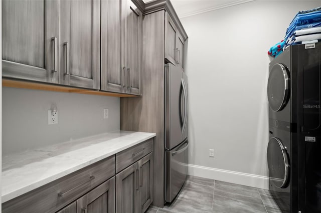 washroom featuring stacked washer / dryer, ornamental molding, light tile patterned floors, and cabinets