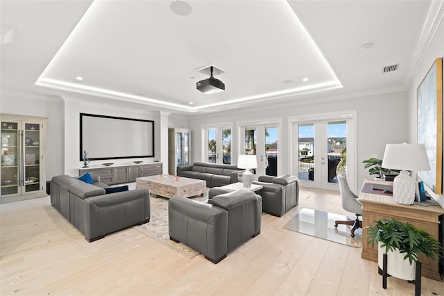 cinema room featuring a tray ceiling, ornamental molding, french doors, and light wood-type flooring