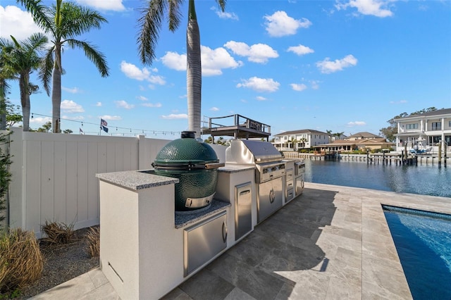 view of patio with grilling area, a water view, and an outdoor kitchen