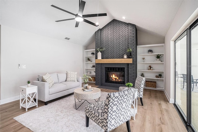 living room featuring built in shelves, vaulted ceiling, a brick fireplace, ceiling fan, and light hardwood / wood-style floors