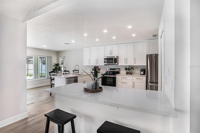 kitchen featuring a breakfast bar area, appliances with stainless steel finishes, kitchen peninsula, light stone countertops, and white cabinets