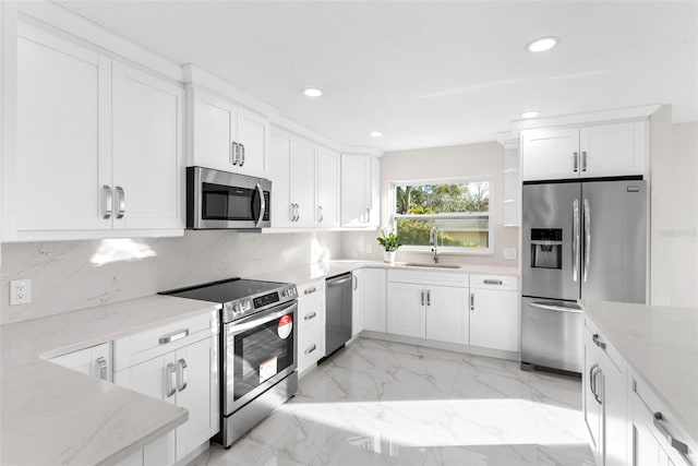 kitchen featuring appliances with stainless steel finishes, white cabinetry, sink, backsplash, and light stone countertops