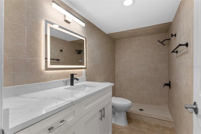 full bathroom featuring tile walls, tiled shower, vanity, and toilet