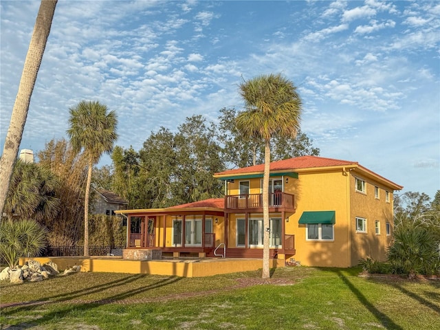 back of house featuring a yard, a balcony, and stucco siding