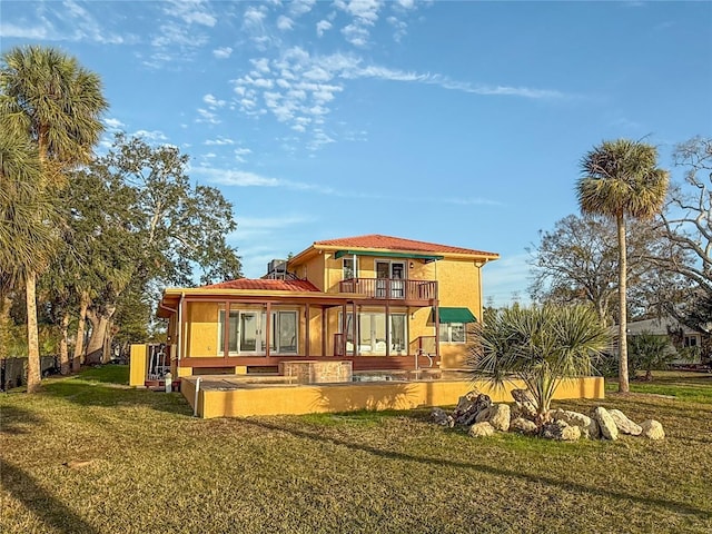 back of property featuring a balcony, a lawn, and stucco siding