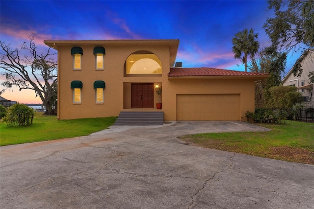 mediterranean / spanish home featuring an attached garage, a tile roof, a yard, concrete driveway, and stucco siding