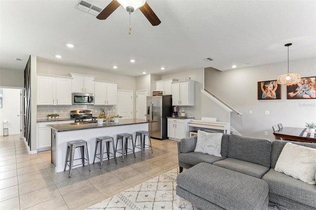 kitchen with a breakfast bar area, appliances with stainless steel finishes, a kitchen island with sink, backsplash, and white cabinets