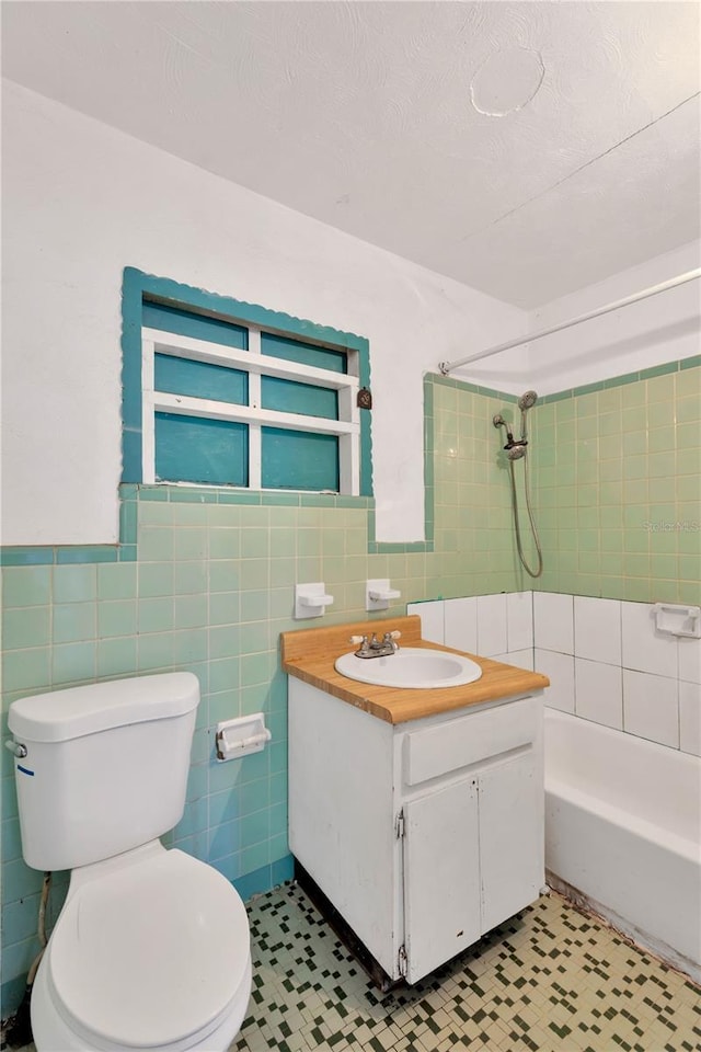 full bathroom featuring tiled shower / bath combo, vanity, tile walls, and toilet