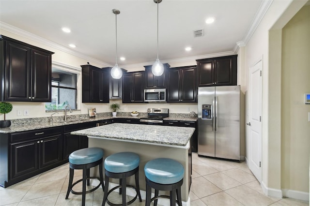 kitchen with sink, appliances with stainless steel finishes, a kitchen island, decorative light fixtures, and light tile patterned flooring