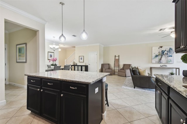 kitchen featuring light tile patterned flooring, crown molding, light stone counters, a center island, and pendant lighting