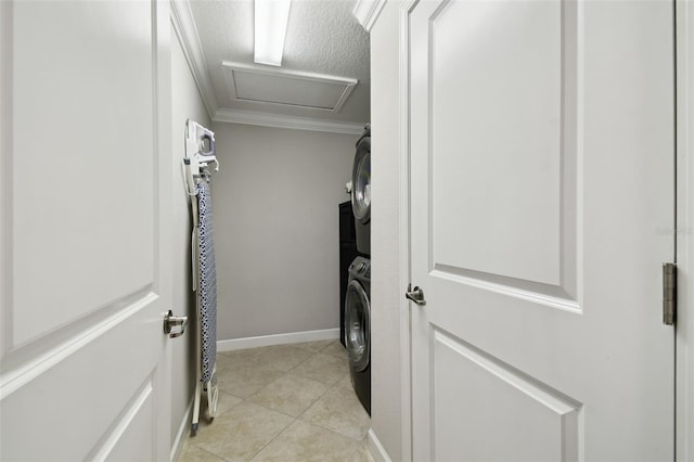 clothes washing area with ornamental molding, stacked washer / drying machine, a textured ceiling, and light tile patterned floors